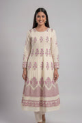A woman modeling a cream-colored Anarkali kurta with pink floral and geometric block prints, paired with matching cream pants, against a solid light pink studio background.